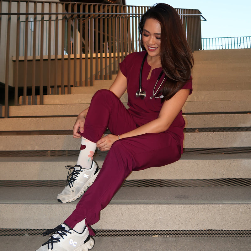 Person wearing maroon pants and white sneakers against a building exterior.