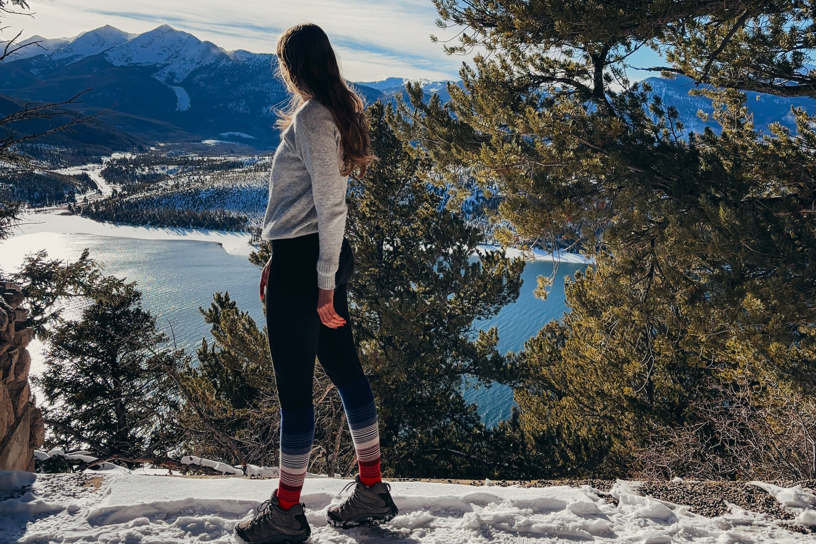 Person standing on a snowy landscape with mountains and a lake in the background