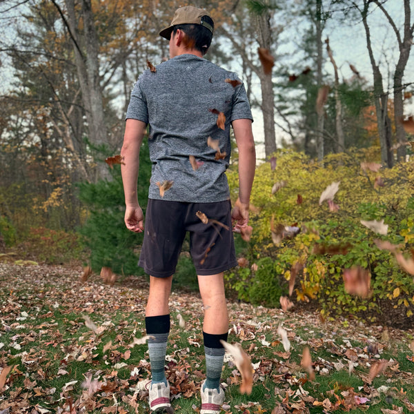 Person walking through a forest with fallen leaves on the ground