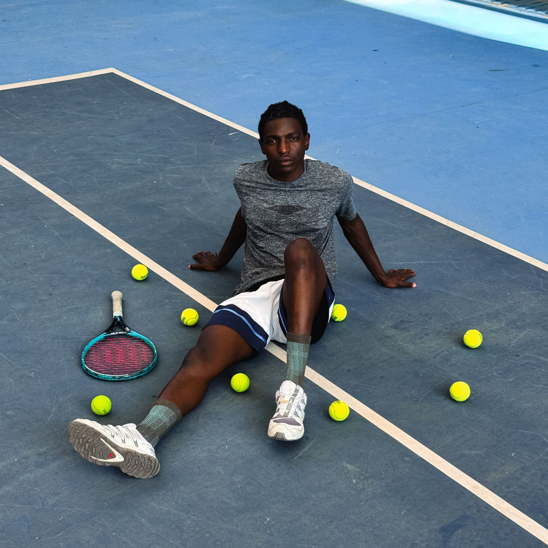 Person sitting on a tennis court with tennis balls and racket